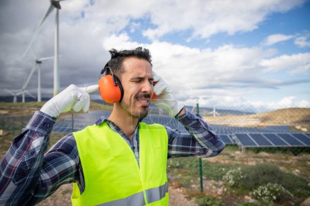 Foto de A Worker suffers from ear pain near wind turbines so he wears noise canceling headphones. - Imagen libre de derechos