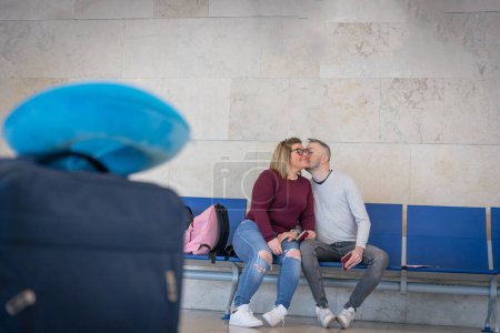 Téléchargez les photos : Un petit ami embrasse sa copine sur la joue pendant qu'ils sont à l'aéroport attendant de voyager - en image libre de droit