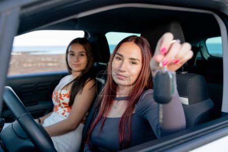 Una joven al volante, sosteniendo las llaves de su coche en la mano y su amiga sentada a su lado