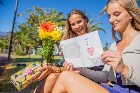 Foto de Hija lee la dedicación escrita a la madre en el Día de la Madre, con los regalos y flores que le dio - Imagen libre de derechos