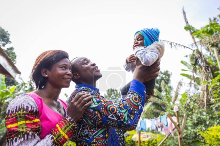 Foto de Un padre eleva a su hijo recién nacido al cielo con su esposa a su lado sonriendo, feliz familia africana - Imagen libre de derechos