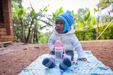 Téléchargez les photos : Mignon africain bébé garçon assis sur l 'tapis et regarder autour. - en image libre de droit