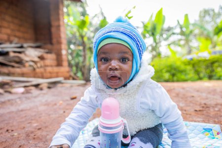Téléchargez les photos : Portrait d'un mignon petit garçon assis sur un tapis dans un village africain. Concept d'enfance heureuse. - en image libre de droit