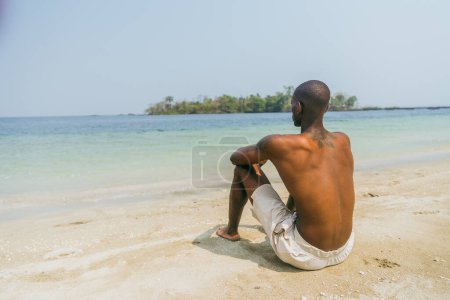 An African boy sitting at the beach relaxes and enjoys his holidays.
