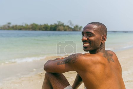Un hombre africano sonriente disfruta de vacaciones en una playa paradisíaca.