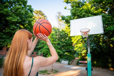 Una mujer lleva a cabo un baloncesto y disparos, estilo de vida deportivo y saludable. La escena se desarrolla en un parque con árboles y bancos