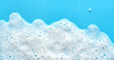 White foam soap sud on blue background. Foam bubbles of detergent fluid gel.