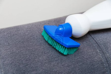 Foto de Limpieza de la casa, limpiador de manchas limpia la superficie del sofá. Agente limpiador con esponja y cepillo - Imagen libre de derechos