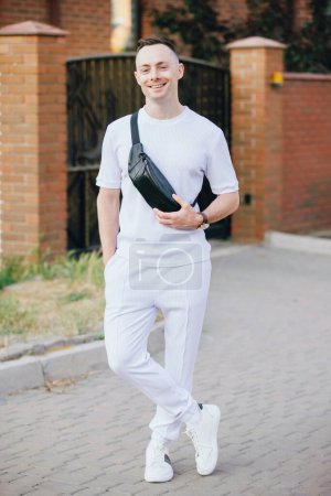 Téléchargez les photos : Élégant homme caucasien en costume blanc posant dans la rue avec sac banane - en image libre de droit