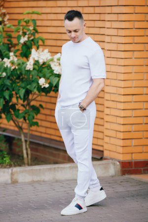 Téléchargez les photos : Bel homme caucasien en costume blanc à la mode posant dans la rue - en image libre de droit