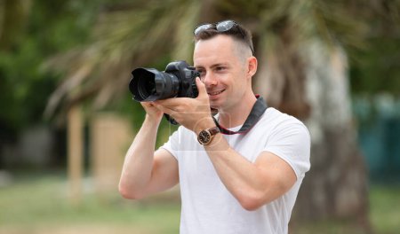Foto de Hombre sonriente fotógrafo tomar una foto en el parque de verano con palmera en el fondo - Imagen libre de derechos