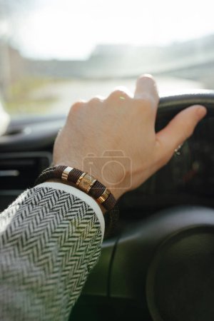 Téléchargez les photos : Une main masculine en blazer, bracelet en cuir dessus, vue depuis le salon de voiture - en image libre de droit