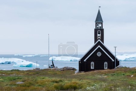 Téléchargez les photos : L'église de Sion est perchée près du front de mer à Illulisat. Derrière des icebergs flottants récemment libérés du massif icefjord voisin. Groenland. - en image libre de droit