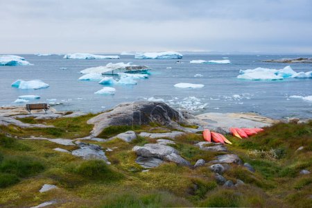 Téléchargez les photos : Un lieu de repos : un banc avec vue sur les icebergs flottant au bord du rivage et une collection de kayaks rouges. Illulisat, Groenland. - en image libre de droit