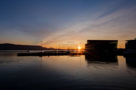 Sonne hinter Bergen in der Nähe von Reykjavik wirft Strahlen über das ruhige Wasser des Alten Hafens und des Harpa Concert Hall & Conference Centre