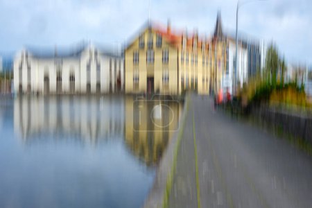 Vertical Intentional Camera Movement (ICM) exagerates some features of colourful buildings near Reyjavik's Tornin Lake while blurring others, including pedestrians.