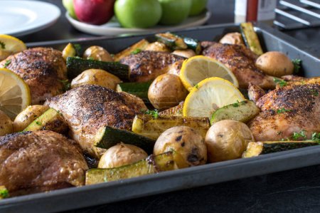 Photo for Healthy homemade dinner or lunch with oven roasted chicken legs, potatoes and zucchini. Served hot and ready to eat on a baking sheet on a dining table at home - Royalty Free Image