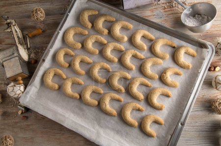 Photo for Fresh and homemade baked vanilla crescents or vanillekipferl. Traditional german or austrian christmas cookies. Served warm on a baking tray on wooden table with old fashioned kitchen utensils. Flat lay - Royalty Free Image