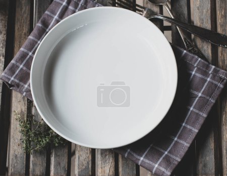 Weißer leerer Teller oder Schüssel auf rustikalem und hölzernem Hintergrund mit altmodischem Löffel und Gabel