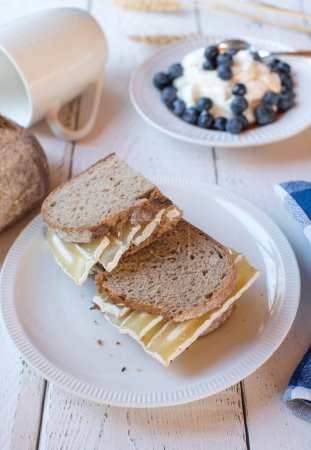 Foto de Healthy breakfast sandwich with sourdough bread and quark cheese. Served with a fresh yogurt and berries on white background - Imagen libre de derechos