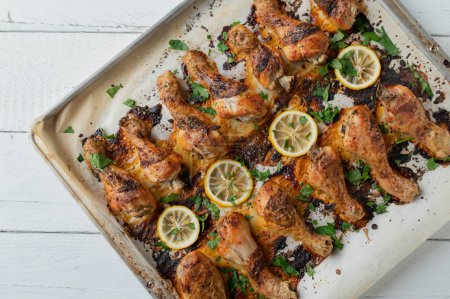 Oven roasted harissa chicken drumsticks on a baking sheet with herbs and lemon isolated on white background. Flat lay
