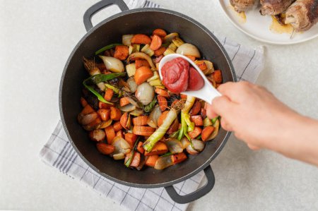 Foto de Put tomato paste in a sauce pan with chopped and roasted vegetables for making sauce or gravy. Part of a seriesCooking, making, preparation of german beef roulades - Imagen libre de derechos
