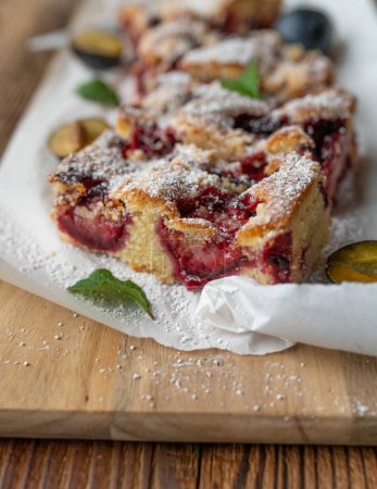 Slice of plum cake with crumbles on wooden cutting board. Selective focus