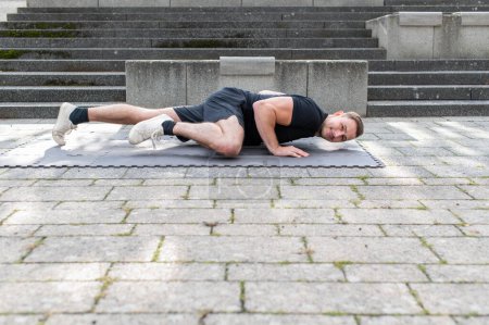 Photo for Young man doing a spiderman push-up or side kick push-up outdoor on floor mat on concrete background. - Royalty Free Image