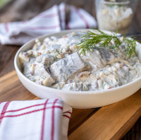Delicious and very tasty german herring salad or heringssalat. Made with pickles, onions, apples and sour cream. Served ready to eat in a bowl on wooden and rustic table background.