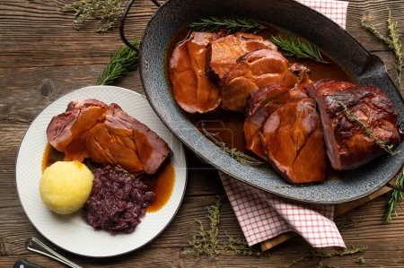 Köstlicher hausgemachter Schweinebraten mit Knödel, Rotkohl und Soße auf rustikalem Hintergrund. Traditionelles deutsches Sonn- und Feiertagsbraten.