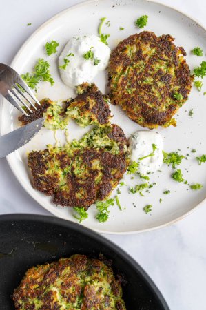 Zucchini fritters with parsley and parmesan cheese on a white plate with dip on light kitchen table background. Top view