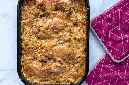 Traditional cuisine or country food with oven baked chicken legs in a very tasty cabbage bacon sauce isolated on light kitchen counter background. Closeup