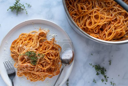 Espaguetis cocinados frescos caseros tradicionales con salsa de tomate sobre fondo de mesa blanco en un plato y en una olla desde arriba.