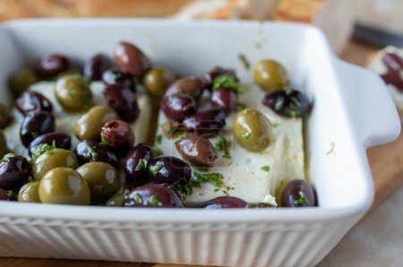 Oven baked feta cheese with marinated black and green  olives in a casserole dish. Closeup with selective focus