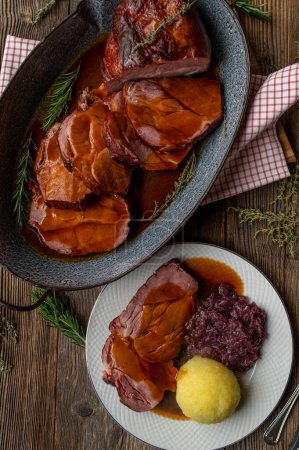 Deutscher Schweinebraten mit köstlicher brauner Soße. Traditionelle und rustikale Küche. Serviert fertig zum Essen in einer Bratpfanne auf Holztischhintergrund.