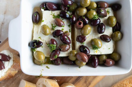 Salade de feta aux olives noires et vertes. Mariné à l'huile d'olive et aux herbes. Servi prêt à manger avec du pain sur fond clair. gros plan