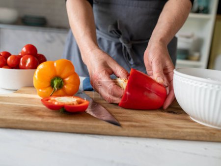 Téléchargez les photos : Creusez un poivron rouge par les femmes main sur une planche à découper dans la cuisine - en image libre de droit