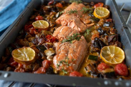 Oven baked half salmon with roasted mediterranean vegetables on a baking tray ready to eat on a table