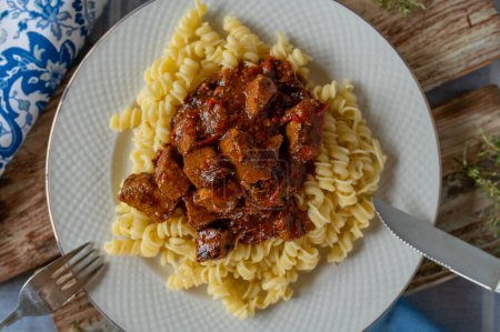 Plate with delicious goulash, hungarian style with pasta isolated on a table. Closeup
