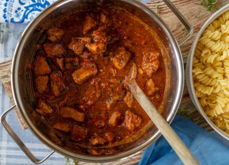 Pork goulash hungarian style with paprika, onions, tomatoes. Served ready to eat in a cooking pot. Closeup