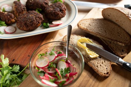 De la nourriture rustique. Dîner avec boulettes de porc frites fraîches, pain au levain, beurre et salade de radis sur table en bois