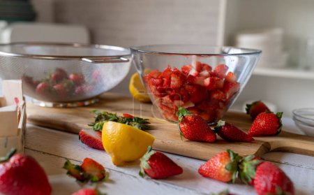Marinated and chopped strawberries in a glass bowl on a cutting board on kitchen counter
