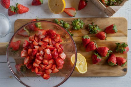 Marinated and chopped strawberries in a glass bowl on a cutting board on kitchen counter