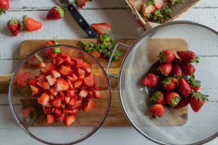 Chopped fresh strawberries in a bowl on a cutting board. Preparing food