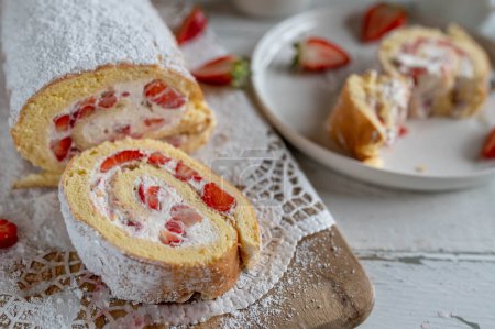 Cake roll with whipped cream and strawberries on white table background