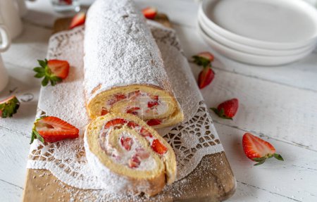 Rollo suizo o pastel roulade con crema batida y relleno de fresa sobre fondo de mesa blanco con decoración.