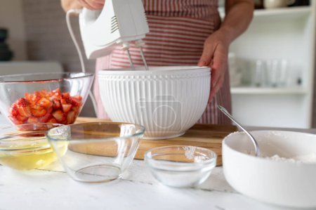 Femme mélangeant pâte ou pâte avec un mélangeur à main pour faire un gâteau aux fraises dans la cuisine.