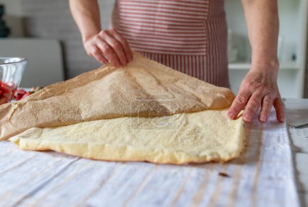 Taking off or removing baking paper from a sponge cake base on a baking sheet by womans hands in the kitchen. Closeup, front view