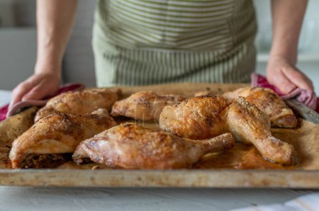 Frau serviert frisch gebackene Hühnerkeulen auf einem Backblech in der Küche. Nahaufnahme, Frontansicht