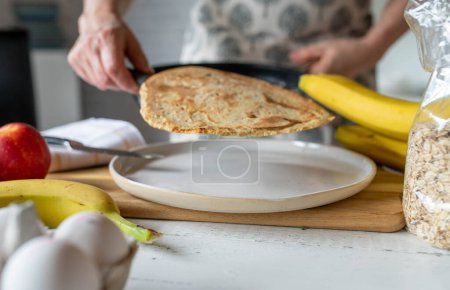 Mujer sirviendo una tortita de avena fresca de una sartén en un plato para un desayuno saludable